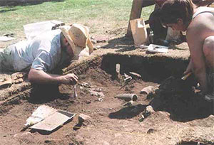 Archaeologists using a brush to expose a bottle broken insitu at the Elizabeth Furnace Plantation Site.