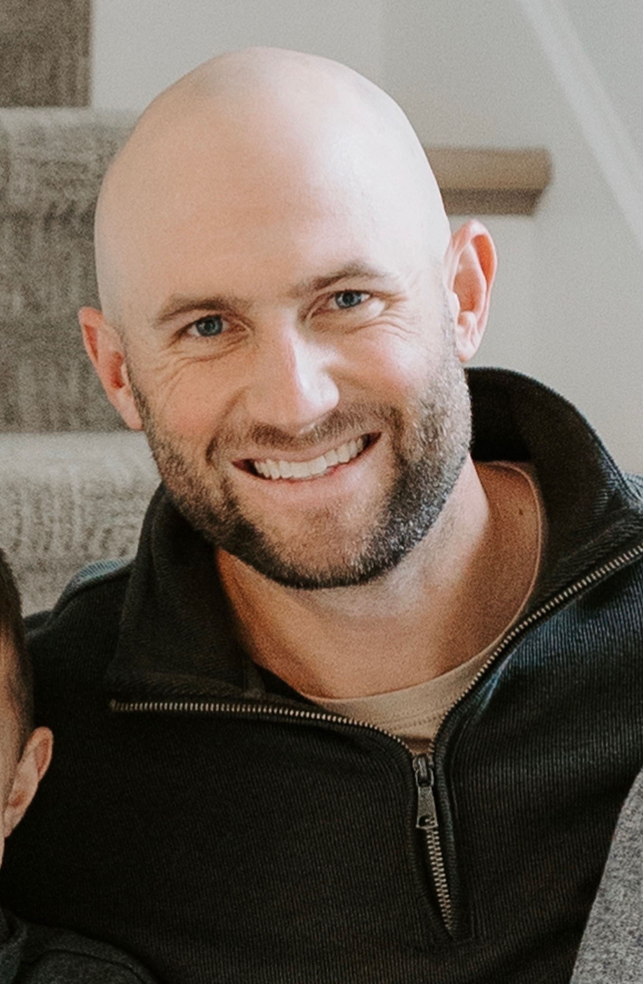 Person wearing a dark zip-up sweater over a beige shirt, seated on carpeted stairs indoors.