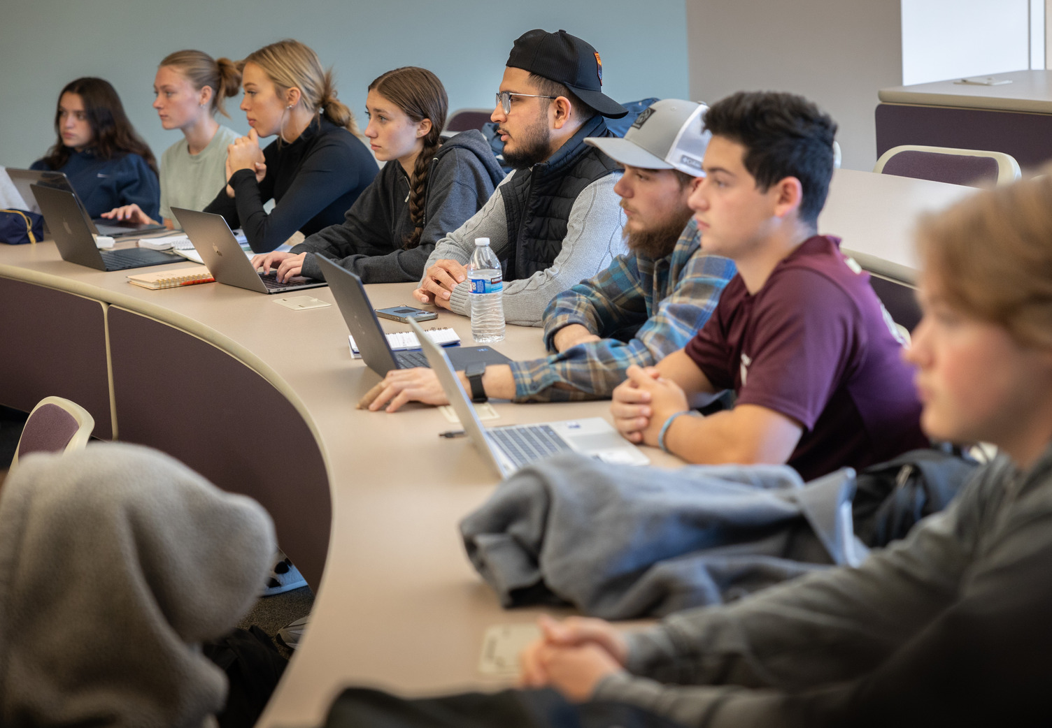 Group of students sit in class and takes notes on computers