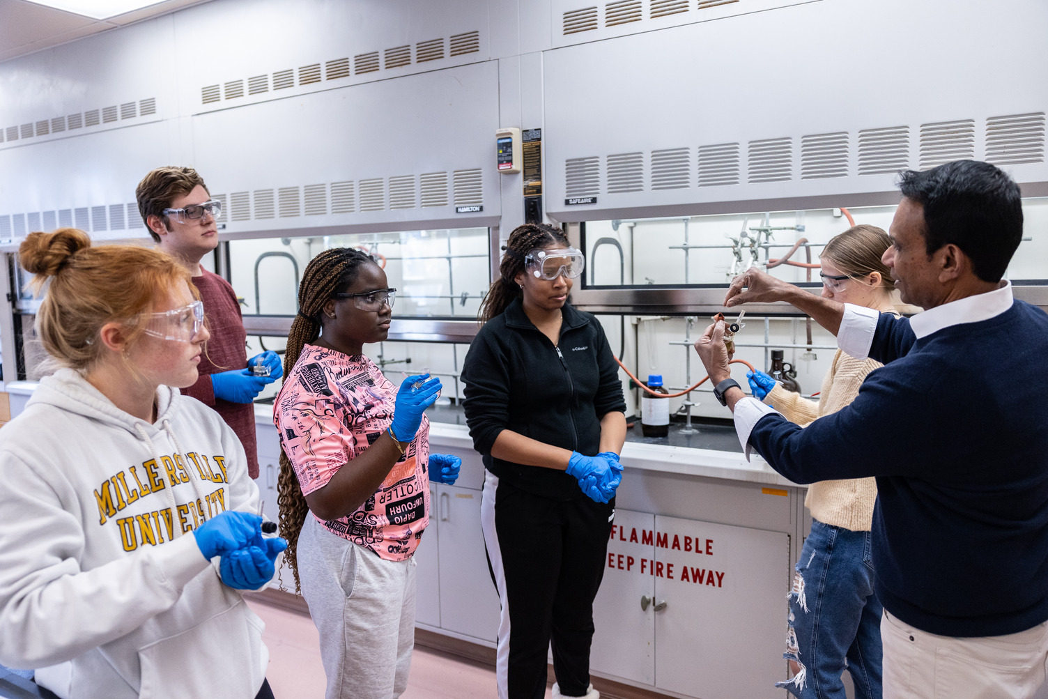 Students in lab surrounding teacher giving instructions