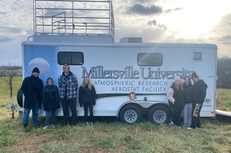 Students standing in front of a weather trailer for research