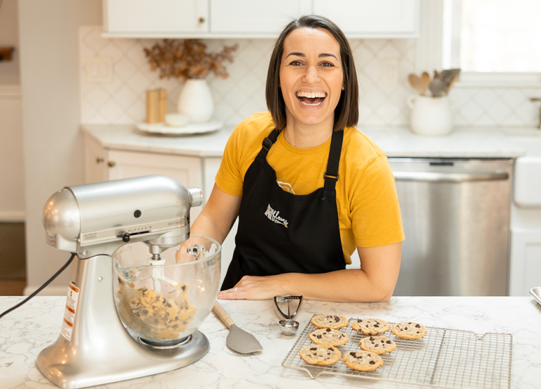 Lynn April, Alumna, stands at kitchen counter baking cookies with stand mixer.