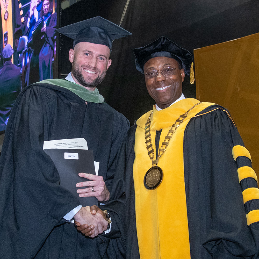 A person in a graduation gown shaking hands with a person in a graduation gown