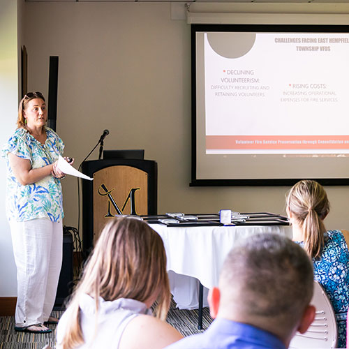 Presenter giving a talk to an audience with a slide projected on the screen.