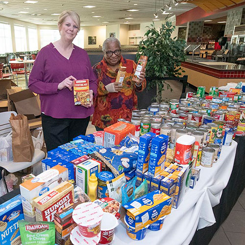 Wendy Bowersox and Virginia Brooks stand behind a table full of donated items for the Campus Cupboard