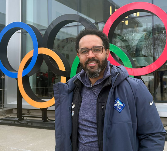 Jean Casimir stands in front of an Olympic rings sculpture, sporting a Beijing 2022 Olympic jacket.