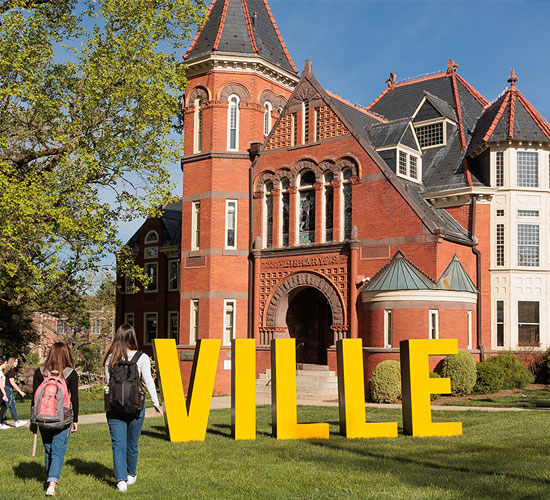 Students walk across the lawn toward a historic red-brick campus building.