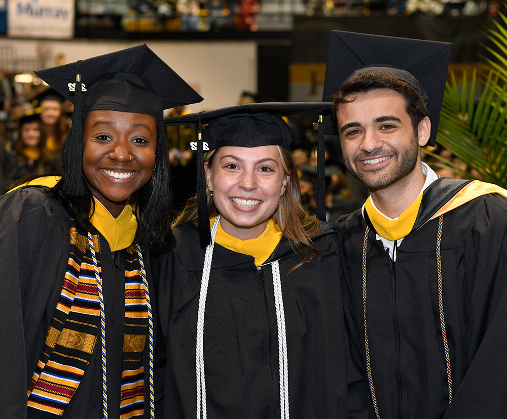 Three students in cap and gown at commencement