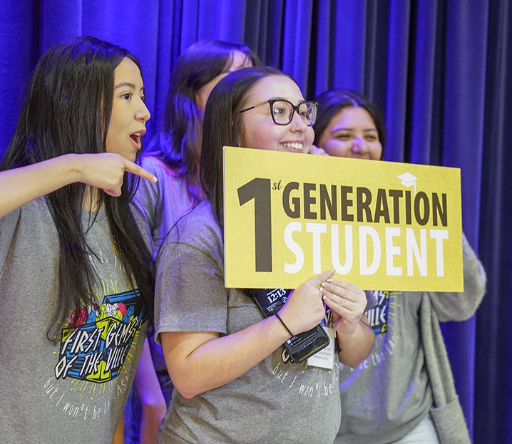 Group of female students holding a sign that says "1st Generation Student"