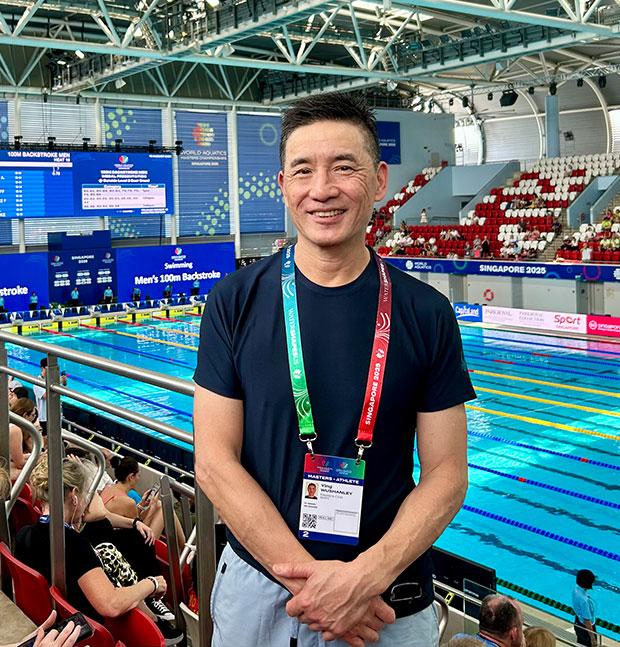 Man standing in front of indoor pool, wearing a lanyard around his neck