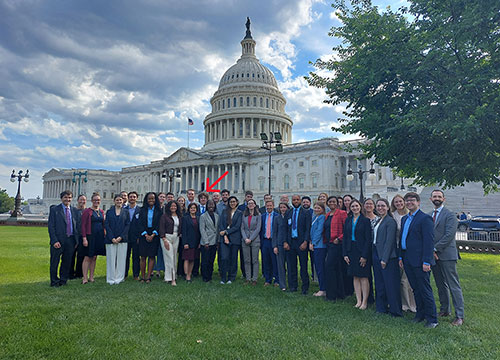 Group photo of people standing on the lawn in front of the U.S. Capitol building.