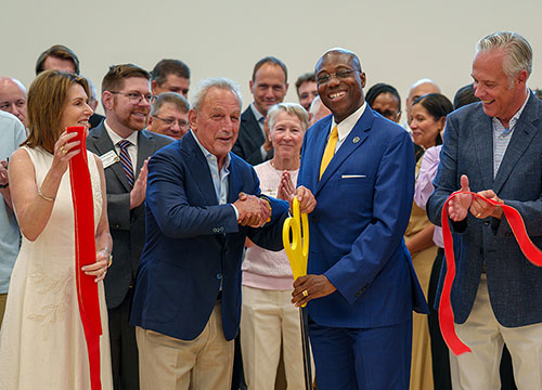 Lombardo Hall Ribbon-cutting ceremony with community members gathered around two people holding oversized ceremonial scissors.